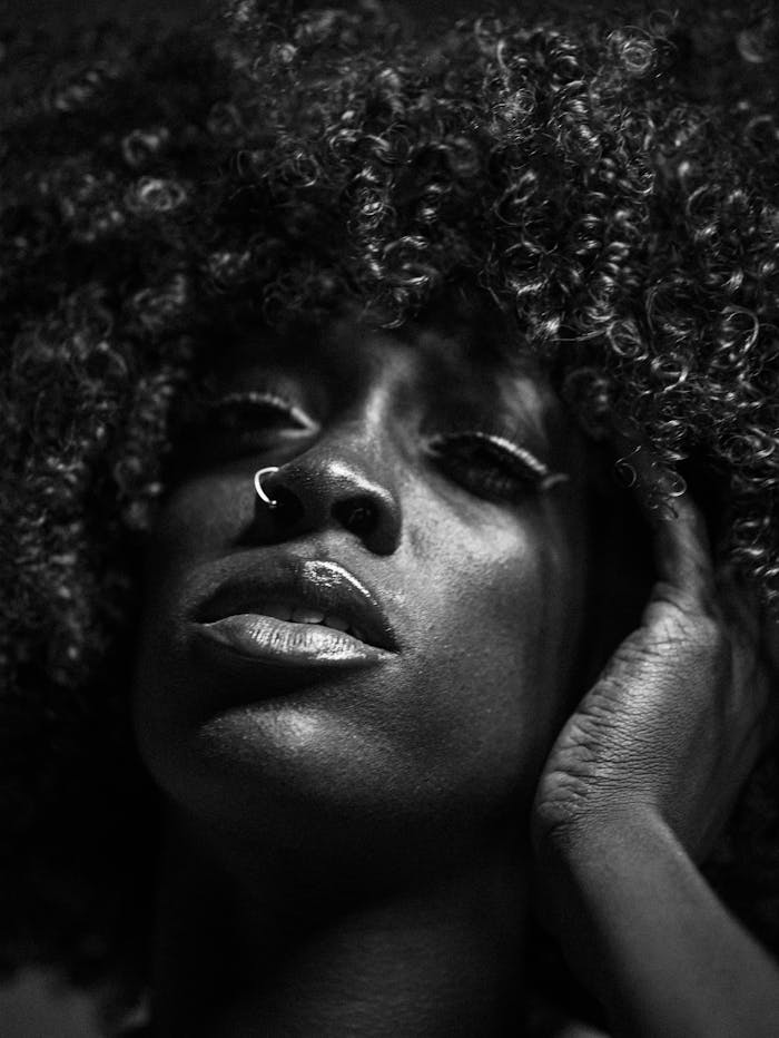 Dramatic close-up black and white portrait of a woman with curly hair and a nose ring.